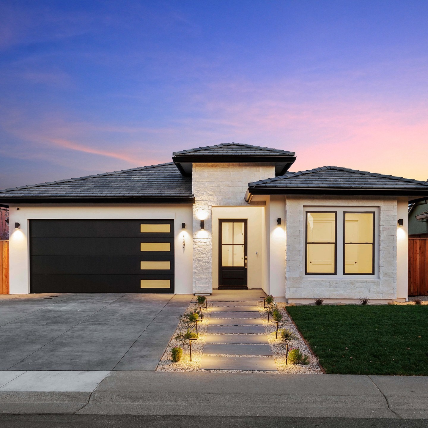A finished single-storey home at dusk, its entry and windows lit.