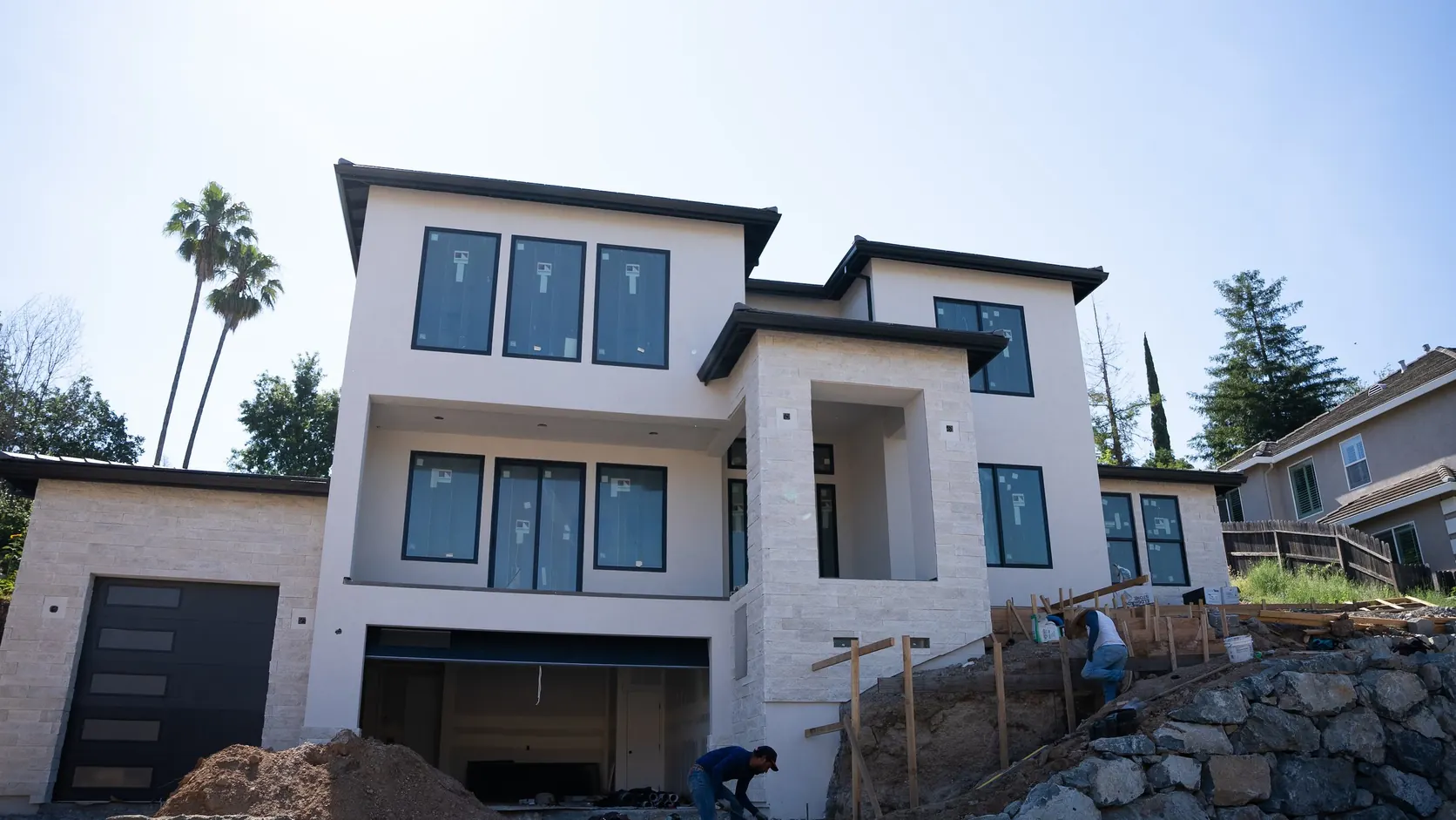 The three storey home nearing completion, white render above stone masonry.