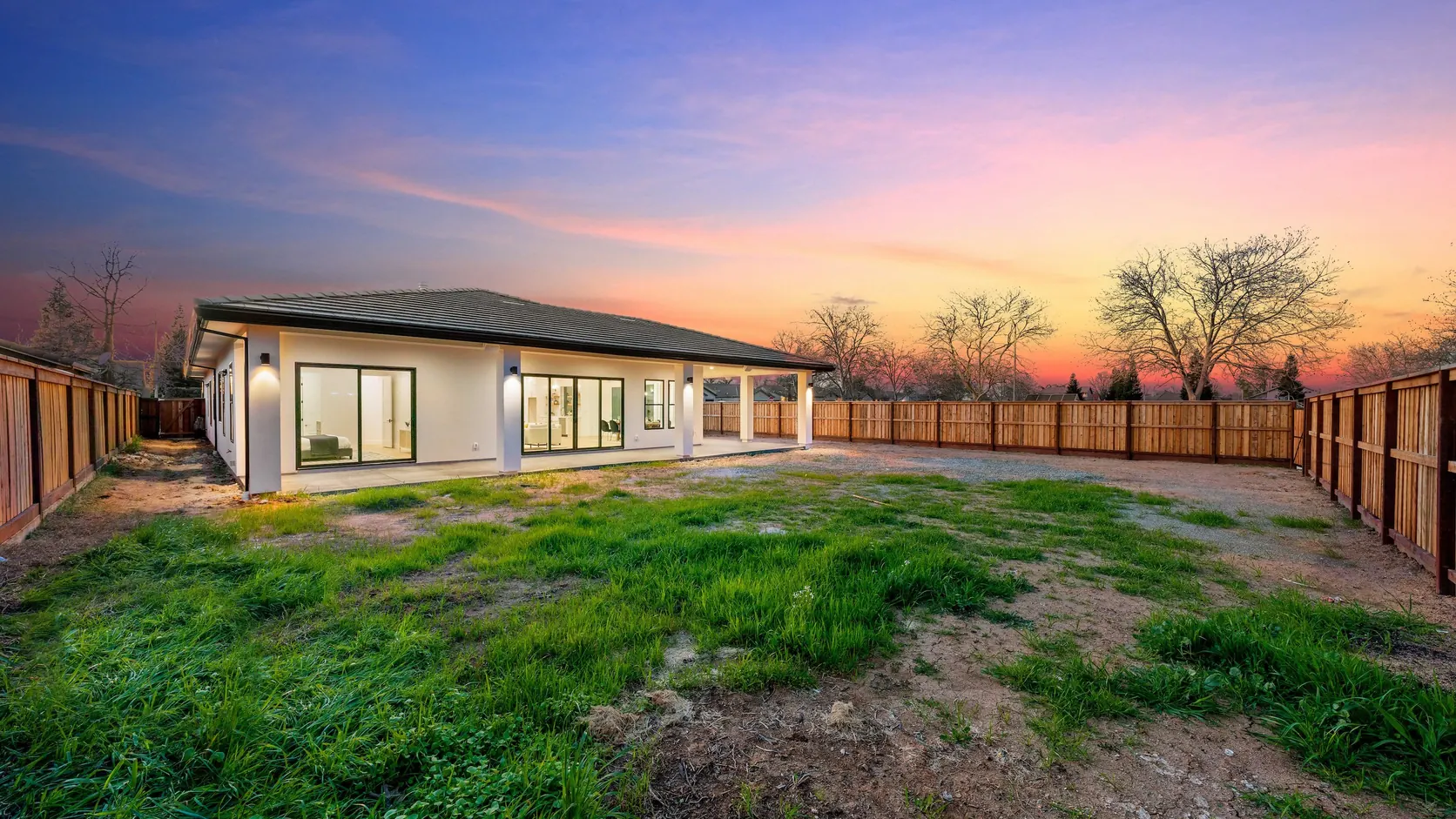 The rear elevation at dusk, glazing lit from within across the back of the house.