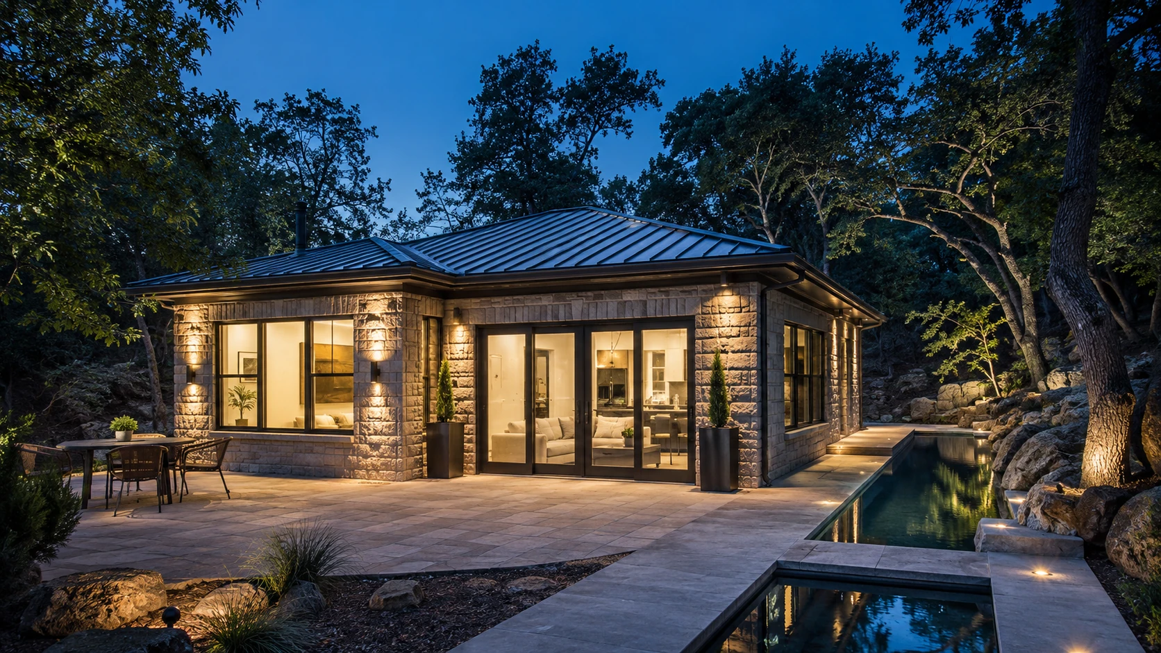 The retreat at dusk, stone-clad under a hipped metal roof beside the pool.