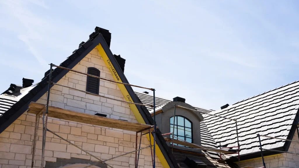 A gable end under scaffolding, stonework and tile in progress.