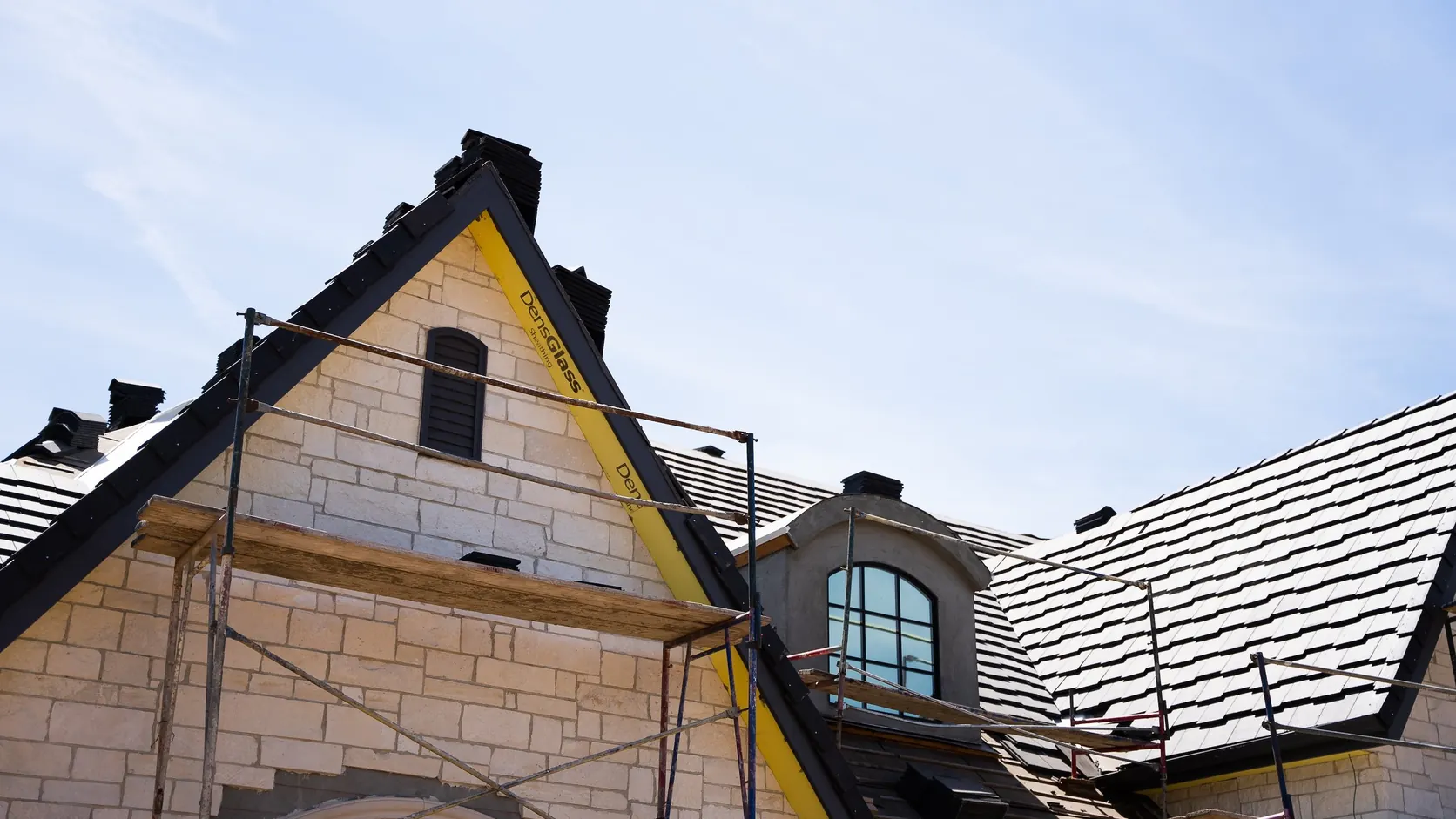 A gable end under scaffolding, stonework and roof tile going on.